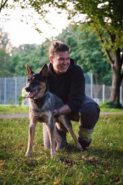 Alexandra Götz kniet lachend auf einer Wiese neben ihrem Australian Cattle Dog Kiano